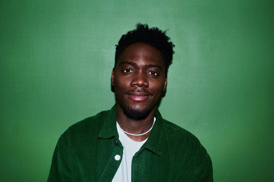 Portrait of young Black man looking at camera against green background, conveying confidence and authenticity. Ideal for diversity marketing, personal branding, profile use