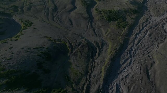 Aerial footage of Koryaksky volcano with snow patches and low clouds drifting above rugged volcanic slopes under blue sky in Kamchatka Krai, Russia