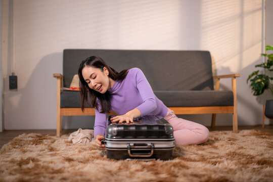 Young woman packing an overpacked suitcase for a trip at home