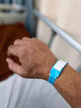 Close-up image of a blue plastic bracelet on the arm of an adult male inpatient in a hospital, a check tape with the admission number and patient identification on the hand of a middle-aged man.