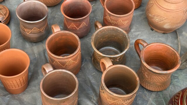 Handcrafted terracotta mugs with intricate traditional patterns displayed for sale, showcasing authentic artisanal drinkware designs