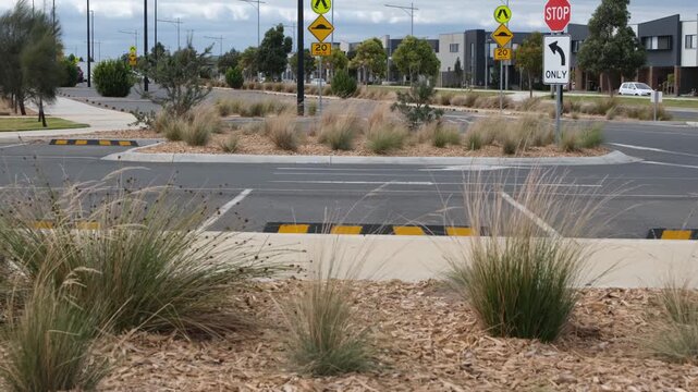 Newly constructed suburban car park in Truganina, Melbourne, featuring wheel stops and drought-resistant native landscaping with ornamental grasses and mulch. Residential townhouses in the distance.