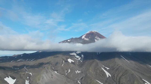 Aerial view of Avachinsky Volcano rising above a low cloud layer, with rocky ridges and snow patches under a clear blue sky in Kamchatka Krai, Russia