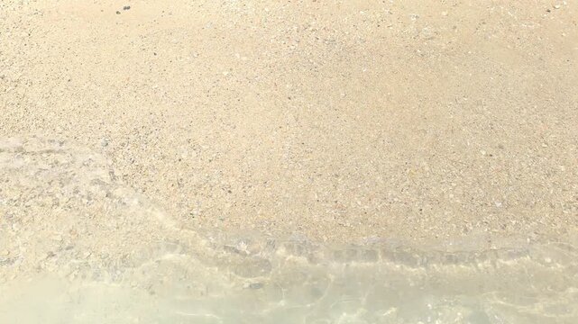 A first person perspective bare female feet in the foaming waves on a light sand beach with small pebbles and shells on a sunny, bright day. Active lifestyle during vacations, holidays, and weekends