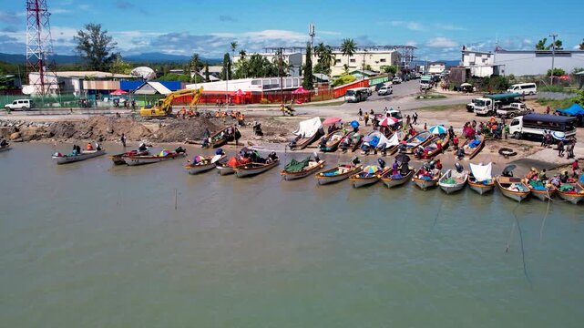 Aerial view of numerous small boats docked along the shoreline with people and construction equipment in Wewak, East Sepik Province, Papua New Guinea.