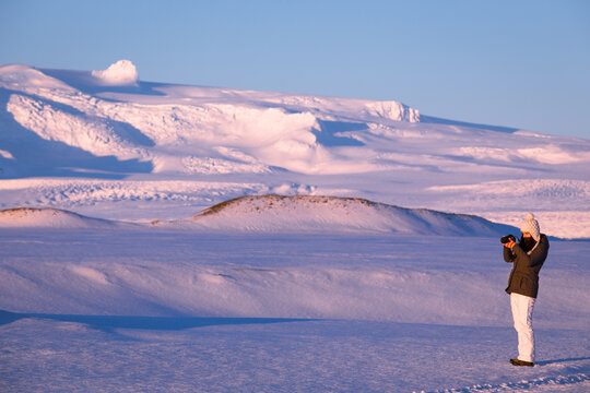 Side view of a teenager girl in warm clothing taking a photo in a remote winter landscape, Iceland