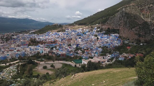 Panoramic view of Chefchaouen, the famous Blue Pearl of Morocco, nestled in the green Rif Mountains under a cloudy sky