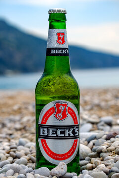 Green glass Beck's beer bottle standing upright on a rocky beach with sea background