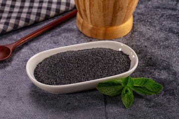 Poppy seeds in white bowl with fresh mint leaf garnish. Culinary ingredient on dark textured background © Andrei Starostin
