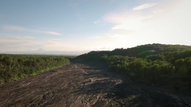 Aerial footage of two off-road vehicles driving along the Sukhaia River dry channel on the route to Avachinsky Volcano, Kamchatka Krai, Russia at sunset