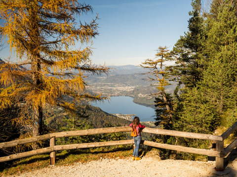 Travel woman enjoying panoramic autumn mountain view over lake and valley from Respiro degli alberi path, Lavarone, Paganella, Trentino, Italy, for lifestyle and exploration.