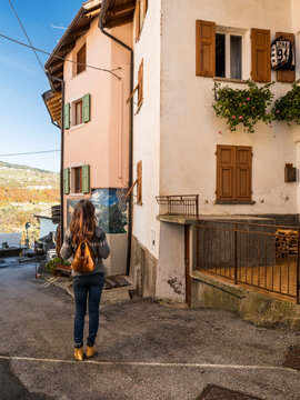 Woman traveler exploring an Italian village street with traditional buildings and a colorful mural, enjoying the outdoor lifestyle in Guardia, Trentino, Italy.
