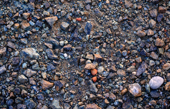 Coarse rocky ground texture featuring sharp fragmented dark gravel and dry dirt