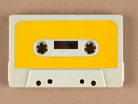 Vue de face d'une cassette audio vintage r&eacute;tro de couleur cr&egrave;me avec &eacute;tiquette jaune. Sur fond uni, concept musical vintage des ann&eacute;es 80.