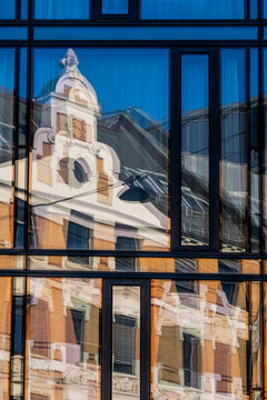 Reflection study where church architecture appears inside modern glass windows on a facade creating symmetry and contrast of historic and modern