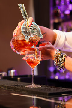 Barman mentre versa un cocktail appena preparato nella coppetta per servirlo al cliente sul bancone del bar