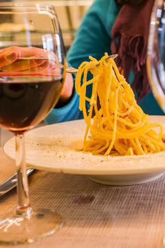 Pasta carbonara con uovo, guanciale e pecorino mentre viene presa con la forchetta da un cliente di un ristorante e con in primo piano un calice di vino rosso