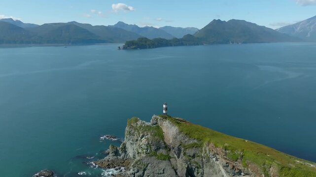 Drone footage of a rocky cape with a small lighthouse in Vilyuchinskaya Bay, with Vilyuchinskaya Sopka volcano and mountain coastline, Kamchatka, Russia