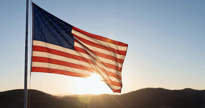 American flag waving proudly against a bright sunset over silhouetted mountains.