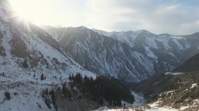 Aerial view of snowy mountain ridges and deep valley with conifer forest at sunrise in Ala-Archa National Park, Chuy Region, Kyrgyzstan, serene winter landscape