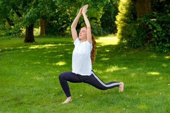 Woman practices yoga in a sunny park during the afternoon while surrounded by trees and green grass