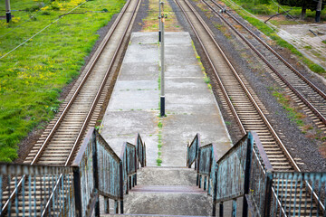 Obraz premium Concrete stairs leading down to an abandoned train station platform with parallel railway tracks stretching into the distance, conveying travel, journey, solitude, and destination