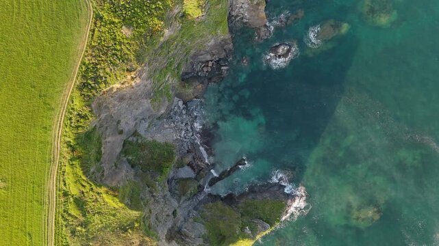 Aerial view of the rugged cliffs and green fields along the South west coastal path near Fowey Harbour with turquoise water and crashing waves, Fowey, England, United Kingdom.