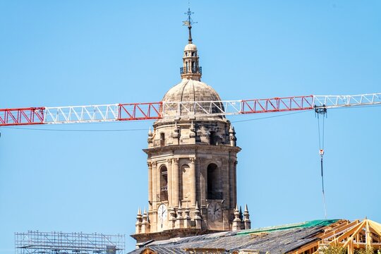 Work on the roof of Malaga Cathedral, installing new tiles on a wooden structure, with a crane passing in front of its iconic single tower