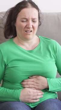 Woman experiencing stomach ache while sitting on sofa at home