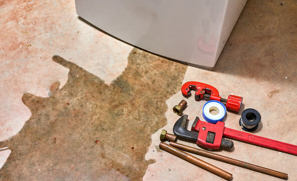 A leaking faucet on a domestic water heater with tools and fittings to replace appliance. Water leaking from the faucet on a residential electric water heater with tools to repair the appliance.