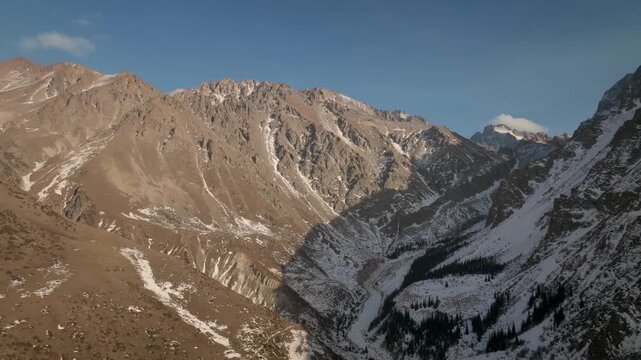 Wide view of rugged snow-dusted mountains and deep valley under clear blue sky in Ala Archa National Park, Chuy Region, Kyrgyzstan, scenic nature travel shot