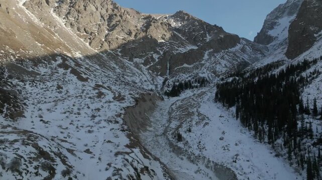 Drone footage of a rugged snowy mountain valley with rocky cliffs and conifer forest in Ala-Archa National Park, Chuy Region, Kyrgyzstan on a clear winter day