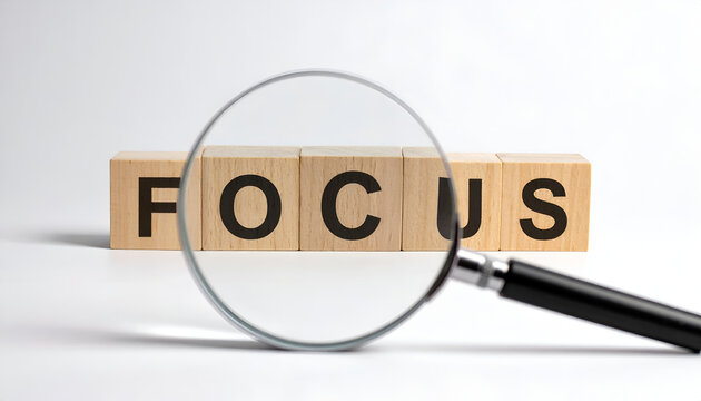 Magnifying glass over wooden blocks spelling out the word FOCUS, symbolizing attention and concentration.