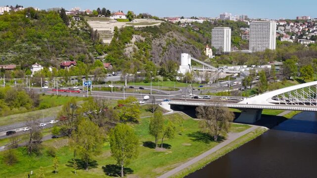 Aerial sunny view of the white Troja Bridge over Vltava river with a red tram and lush green park in Prague