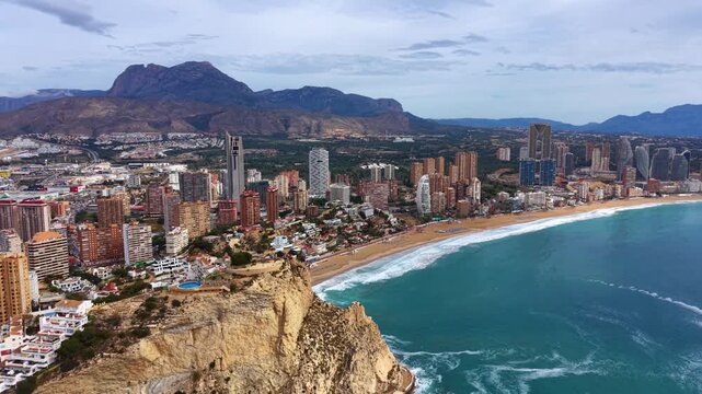 Panoramic view of Benidorm, Spain, showcasing skyscrapers along a sandy beach, turquoise Mediterranean sea, dramatic cliffs and mountain backdrop
