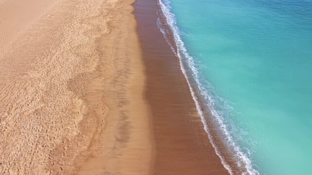 Overhead view of a pristine sandy beach meeting turquoise ocean waves, with golden sand and white sea foam forming a natural boundary between land and sea