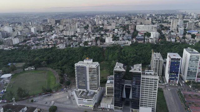 Drone orbits left in downtown separated by large green park on hill during sunset in Maputo, Mozambique