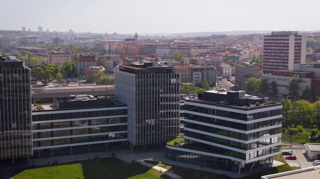 Cinematic aerial view of modern office buildings and Holesovice train station area with Prague city skyline and Zizkov Tower on a sunny day