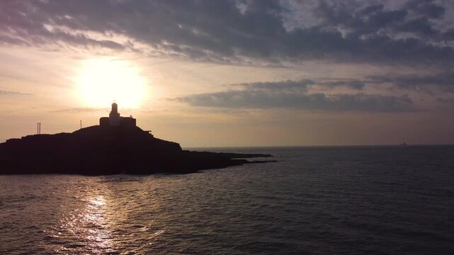Slow Pushing Aerial of Mumbles Lighthouse at Sunrise. Golden Reflection of Sun on Ocean with Dynamic Clouds. Perfect for tourism, travel documentaries. Wales, UK. 4K.