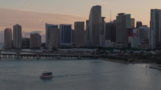 Small ferry boat sailing on the bay with the miami downtown skyline and bayside marketplace at sunset