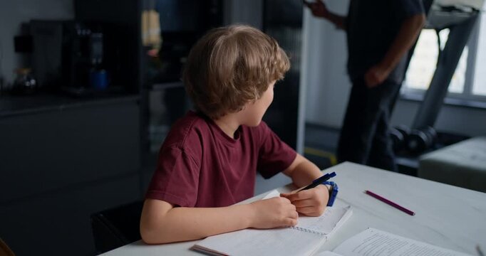 Parent Assists Child With Studies. Parent Supports Son During Focused Homework In Contemporary Kitchen