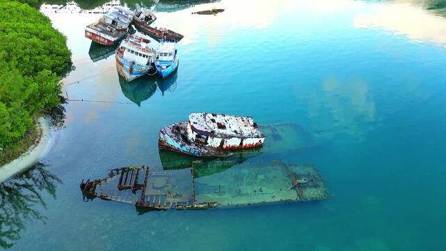 Aerial view of rusted shipwrecks in calm turquoise waters surrounded by lush mangroves in Sandy Bay, Bay Islands Department, Honduras.