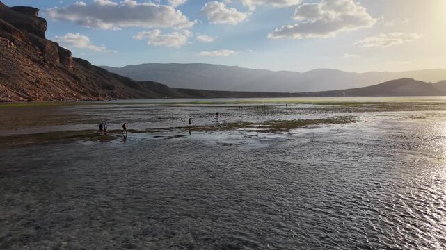 People Walking Across Reflective Tidal Flats at Sunset. Detwah Lagoon, Sokotra, Yemen.