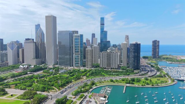 Stunning aerial panorama of Chicago downtown skyline featuring modern skyscrapers along Lake Michigan shoreline with yacht harbor and lush green Grant Park on a sunny summer day.