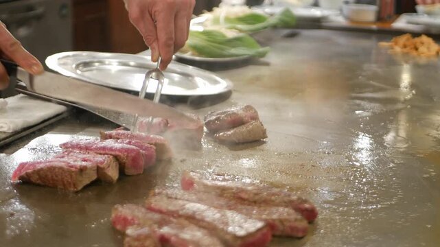 POV to kobe sirloin wagyu steak while cooking on teppan yaki flat pan in japanese style restaurant for lunch time. Chef cooking wagyu kobe beef sirloin steak on teppanyaki flat pan