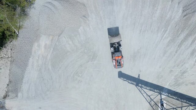 Aerial view of an orange wheel loader moving piles of grey aggregate at the Foamed Glass UK Industrial Factory in Great Heck, England, United Kingdom.