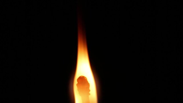A tall thin match flame on black background: starts as wide bright orange fire, narrows into tall slender red-orange column, then gradually shrinks and dims.