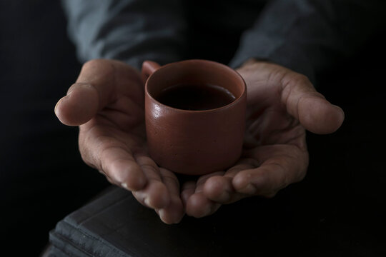 Person holding a small cly cup over s teapot