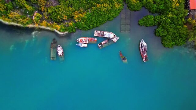 Aerial view of abandoned and sunken boats in turquoise water along the lush mangrove shoreline of Sandy Bay, Bay Islands Department, Honduras.