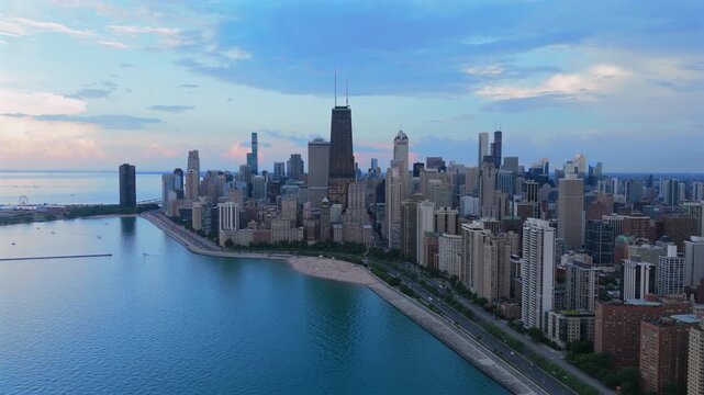 Stunning aerial footage of Chicago downtown skyline along Lake Michigan waterfront during evening twilight. Skyscrapers and high-rise buildings line the shore with sandy beach visible below.